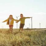 Little girl and boy are running in front of windmills.