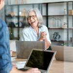 Happy mature old female mentor coach supervisor training young interns at group office meeting professional workshop.