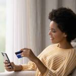 Happy young African American woman holding cellphone and bank credit card in hands