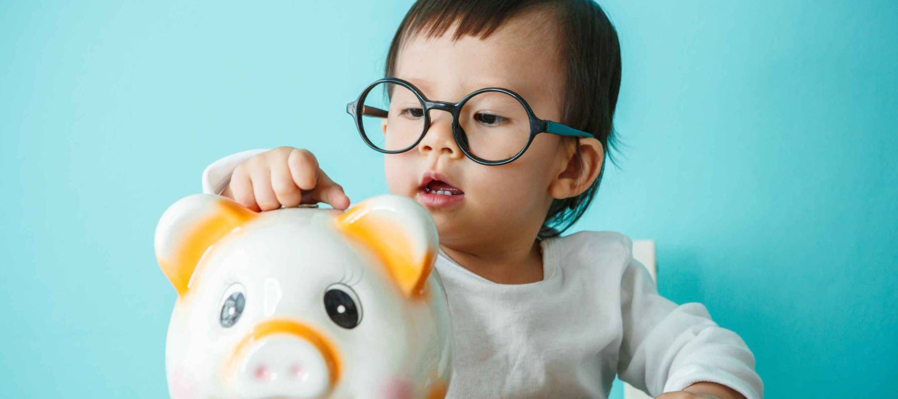Baby child putting a coin into a piggy bank, kid saving money for future concept
