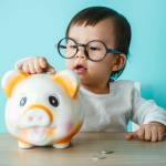 Baby child putting a coin into a piggy bank, kid saving money for future concept