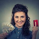 Young woman shopping holding showing credit card and cash dollar banknotes bills