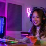 Gamer girl with neon light background, dark room, smiling at credit card with headphones on. cryptocurreny and gaming