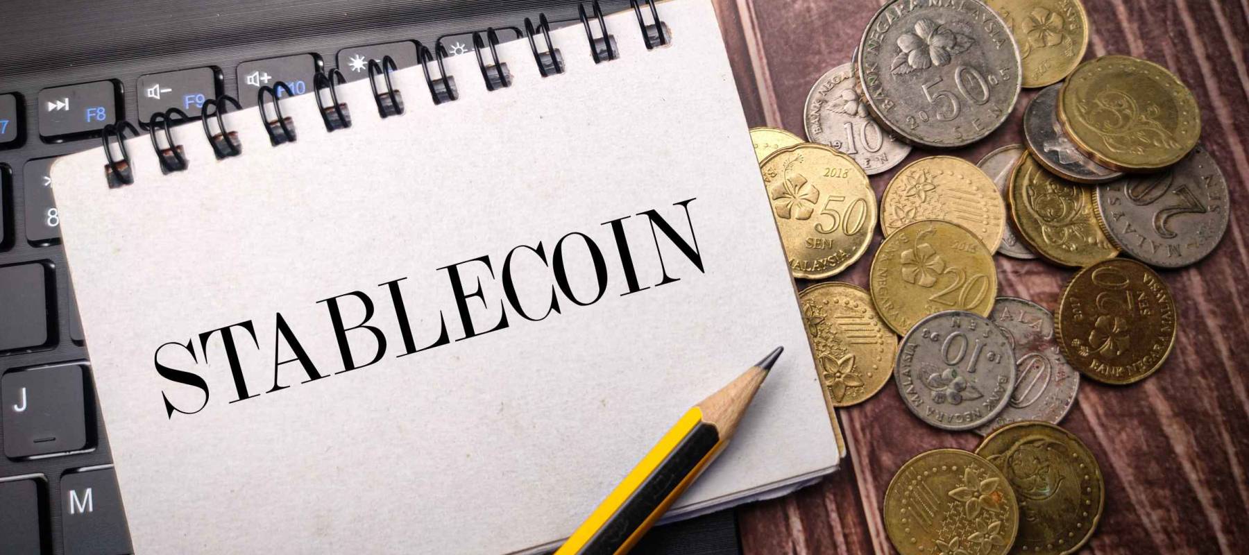 Notebook and coins on a wooden background with the word STABLECOIN.
