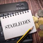 Notebook and coins on a wooden background with the word STABLECOIN.