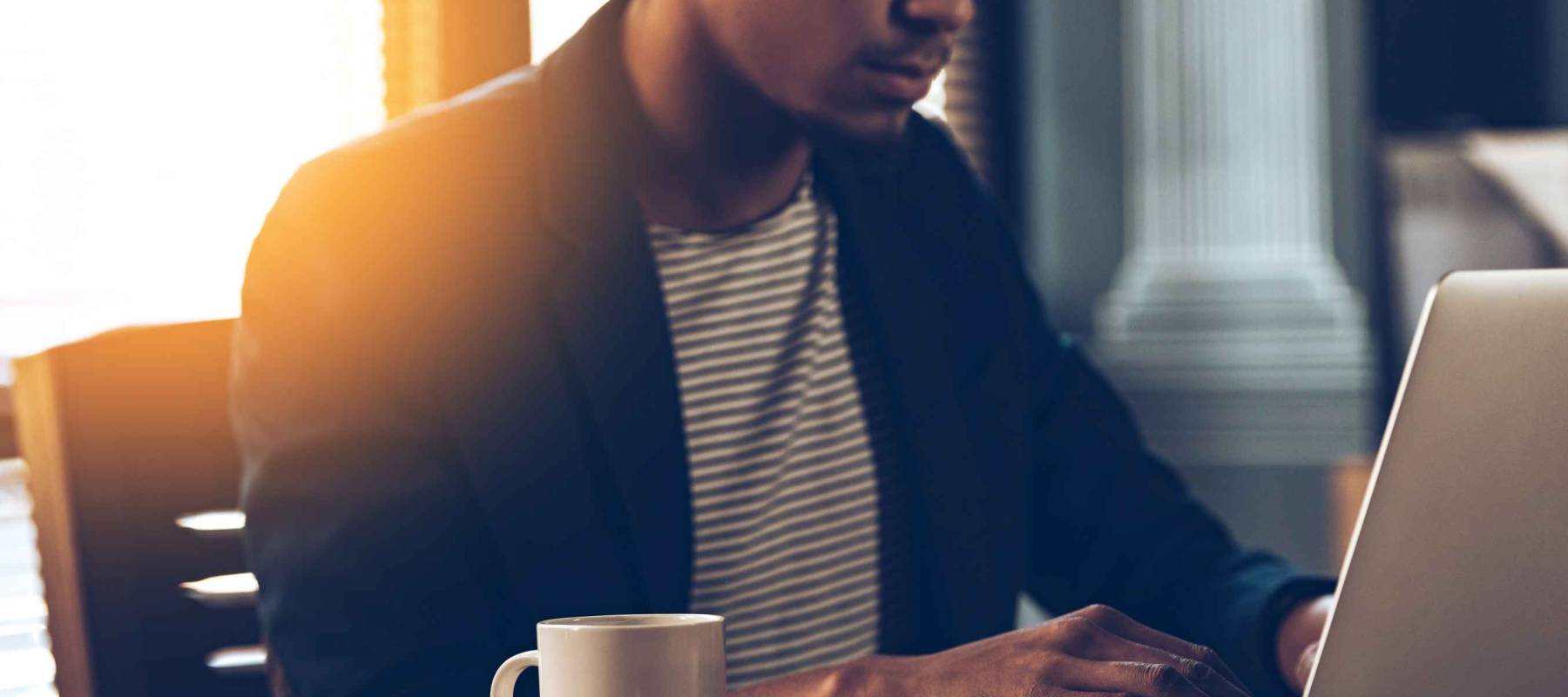 Full concentration. Close-up part of young African man using laptop while sitting at his working place