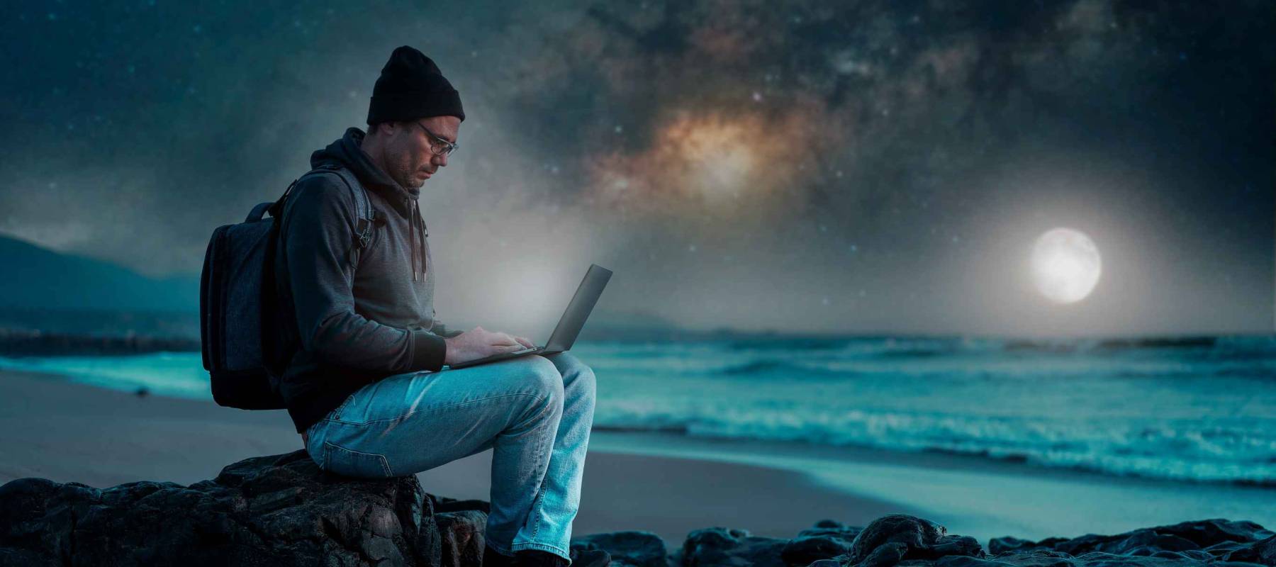person sitting with laptop on the beach outdoors working under the starry night and milky way