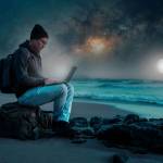 person sitting with laptop on the beach outdoors working under the starry night and milky way