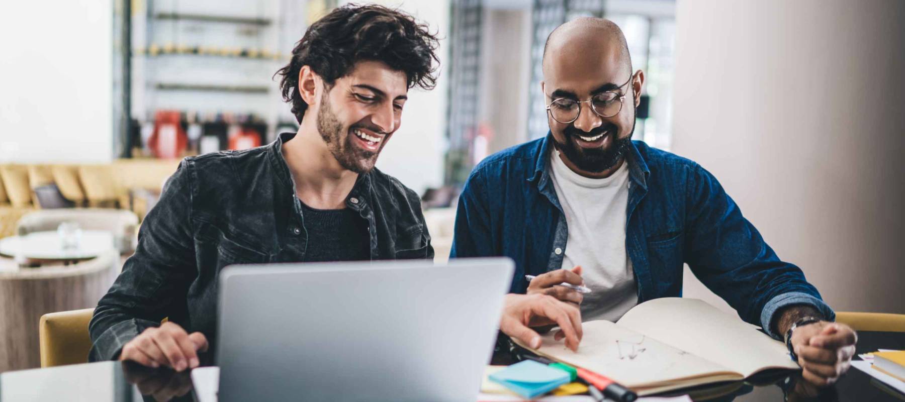 Happy Middle Eastern graphic designers discussing creative sketches during collaborative brainstorming in modern coworking space, cheerful small owners planning together business projecting