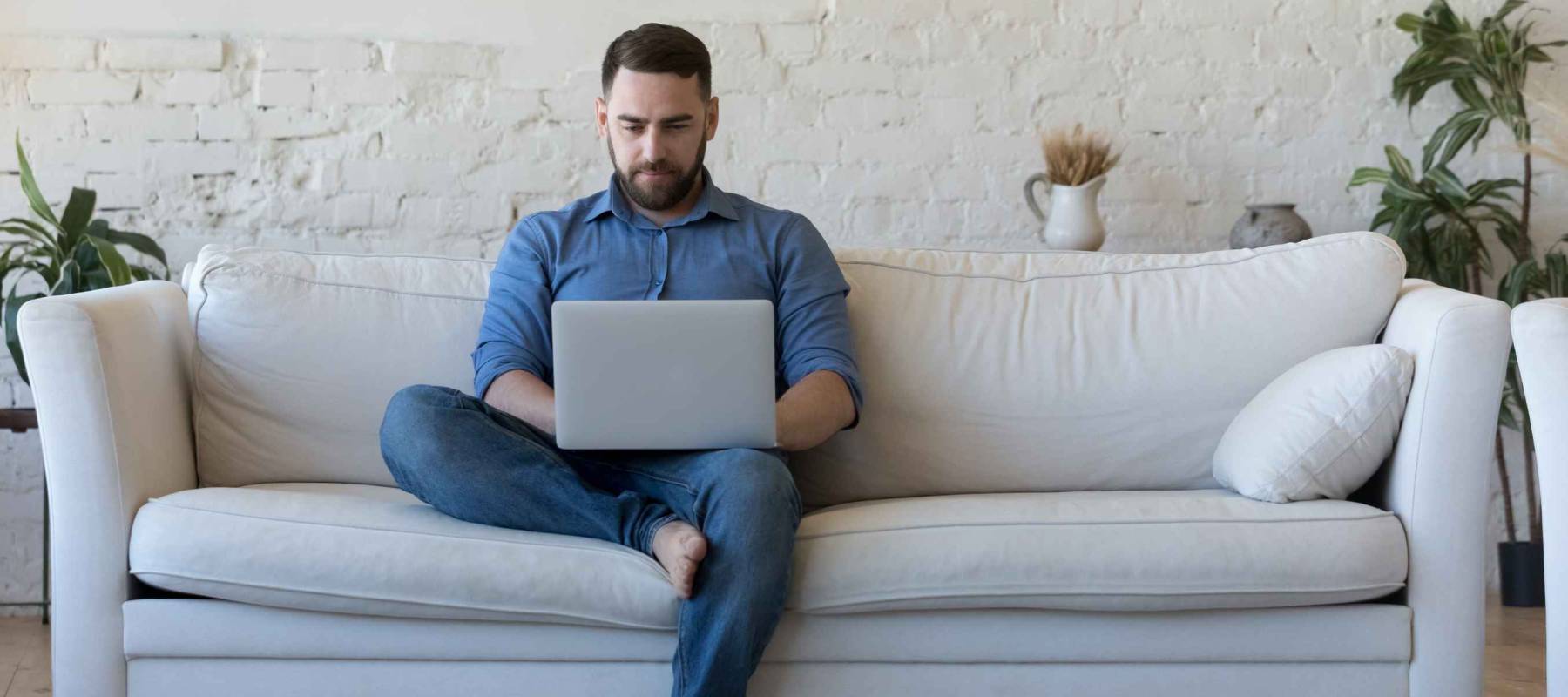Handsome serious man sits on sofa with computer on laps