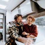 Happy travel couple lifestyle smile and use laptop together inside a modern camper van in vanlife offgrid alternative office workplace.