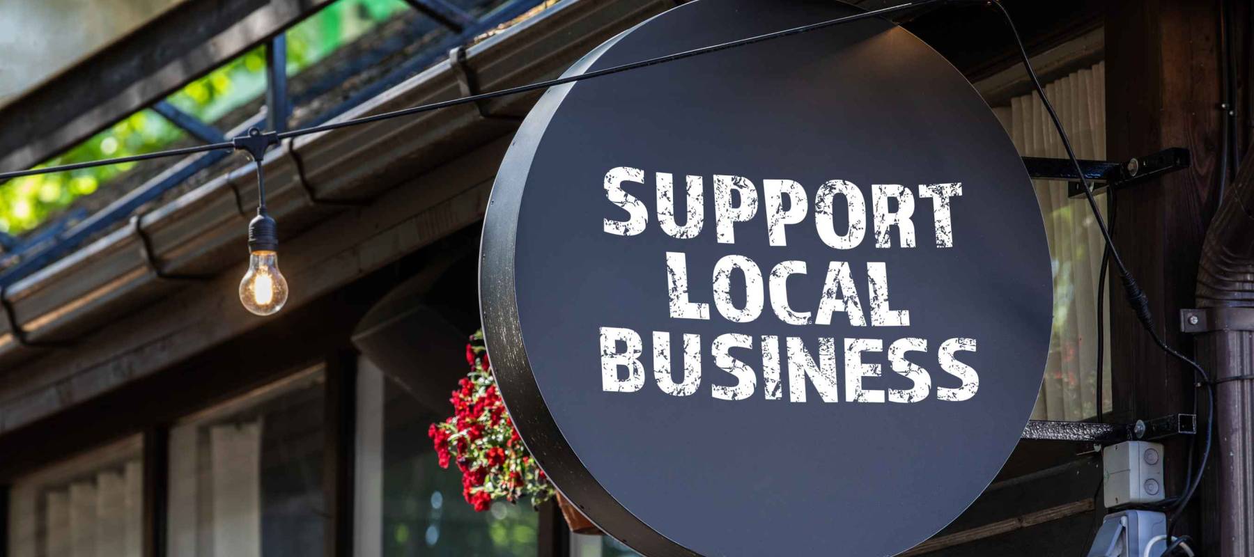 Support local business. Round, black sign onn teh wall of the house.
