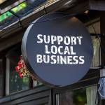 Support local business. Round, black sign onn teh wall of the house.