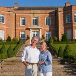 Wide shot of a elderly couple standing together in front of a luxurious estate.