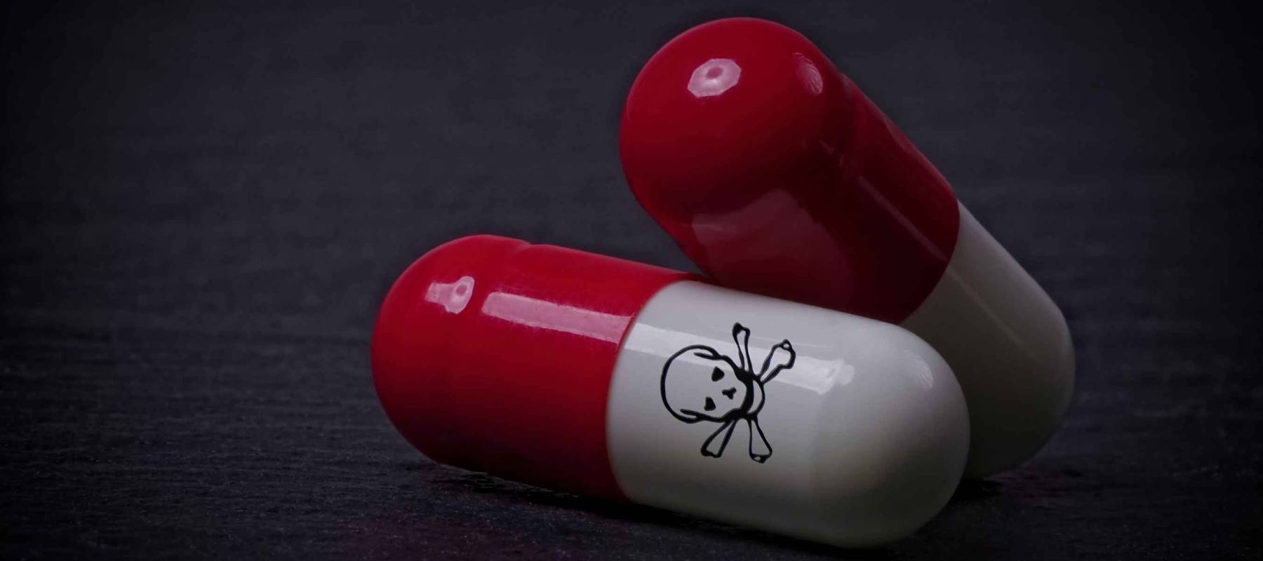 Drug capsules with skull and crossbone on dark stone background.