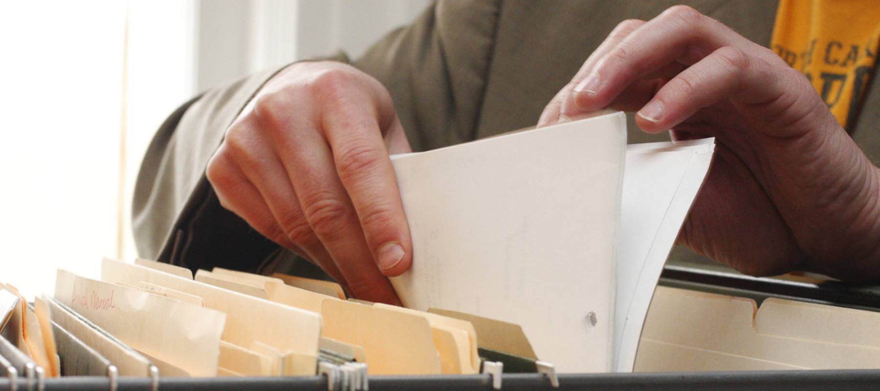Close up of hands sorting through paperwork in a filing cabinet.
