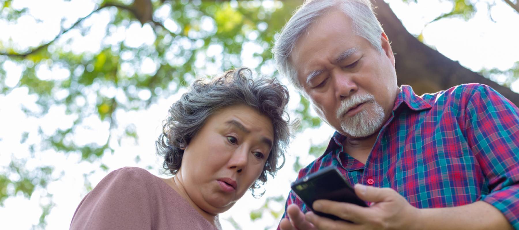 Older couple looking down at phone, shot from below, looking stressed.