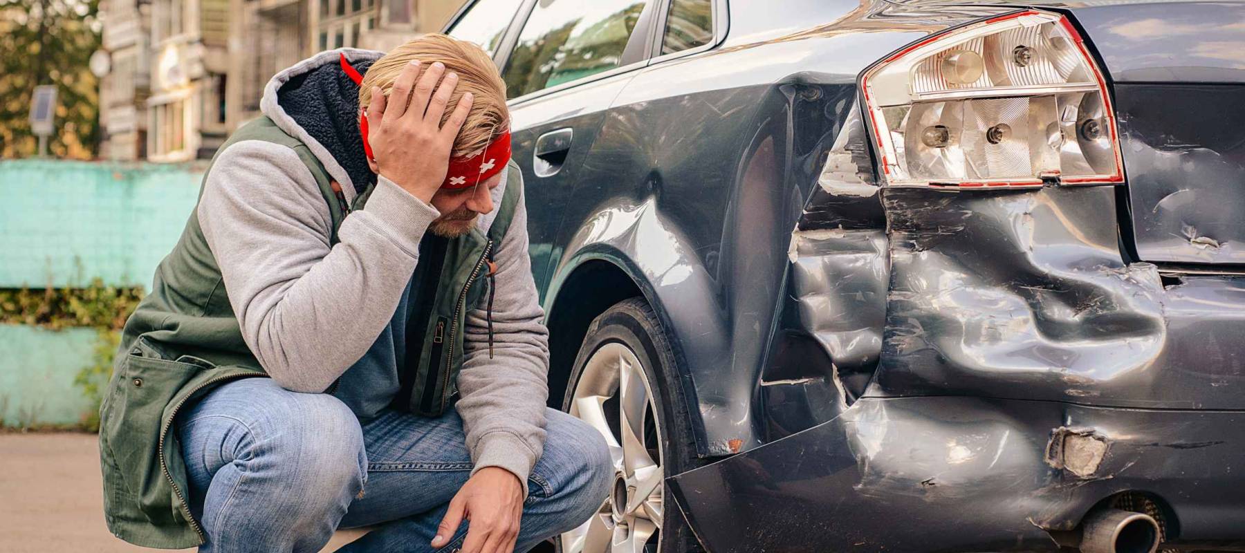 Guy sitting near the wrecked car after the accident, clutching his head.