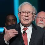 Warren Buffett speaks on stage, making hand gestures.