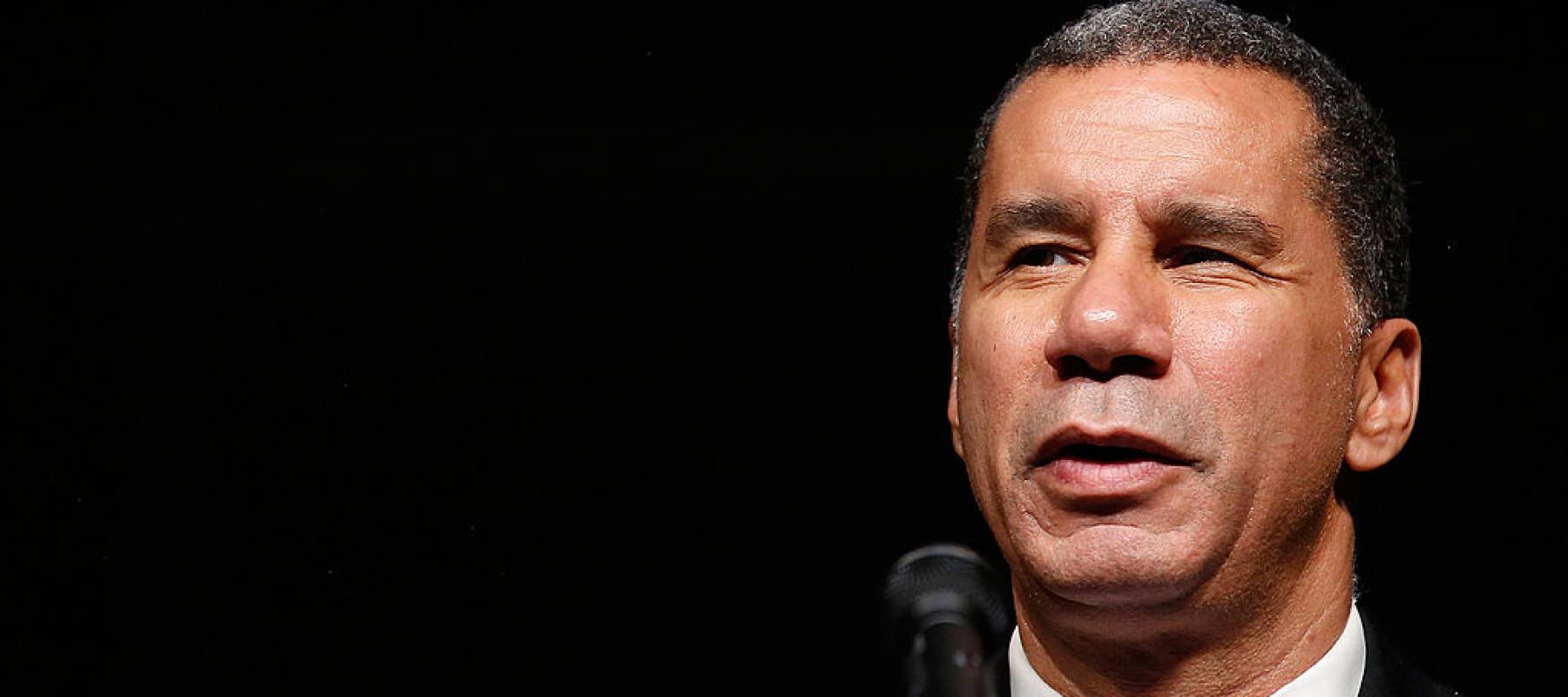 Close up of David Paterson's face while speaking on stage, the background is dark.