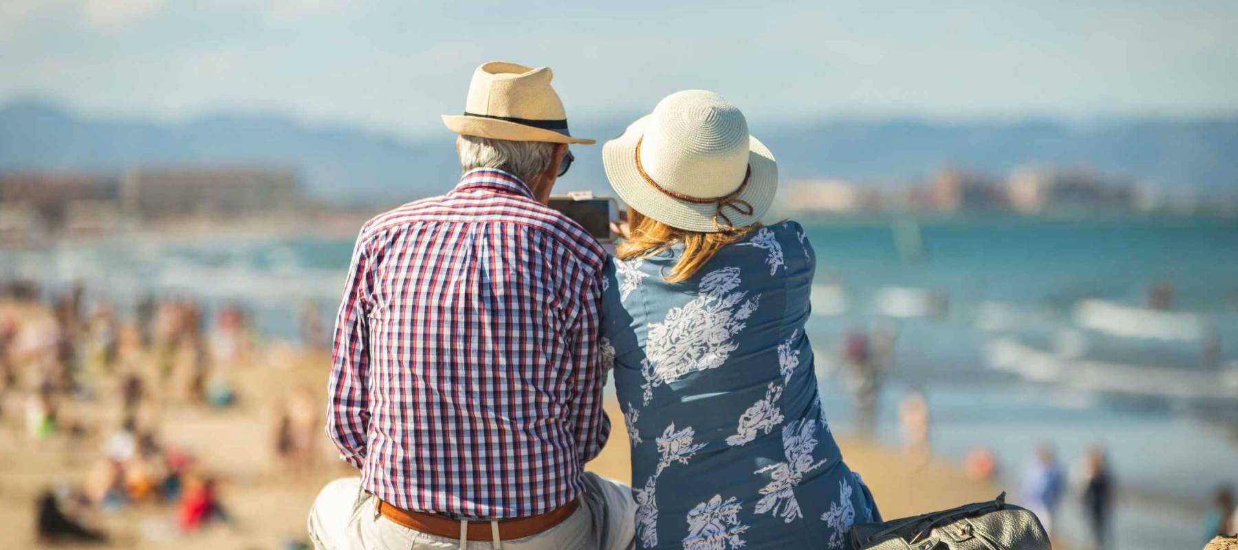 Mature couple of retired lovers enjoying retirement on the beach facing the sea with mobile cell phone taking pictures at sunset. Couple happy true love in the nature
