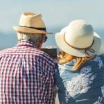 Mature couple of retired lovers enjoying retirement on the beach facing the sea with mobile cell phone taking pictures at sunset. Couple happy true love in the nature