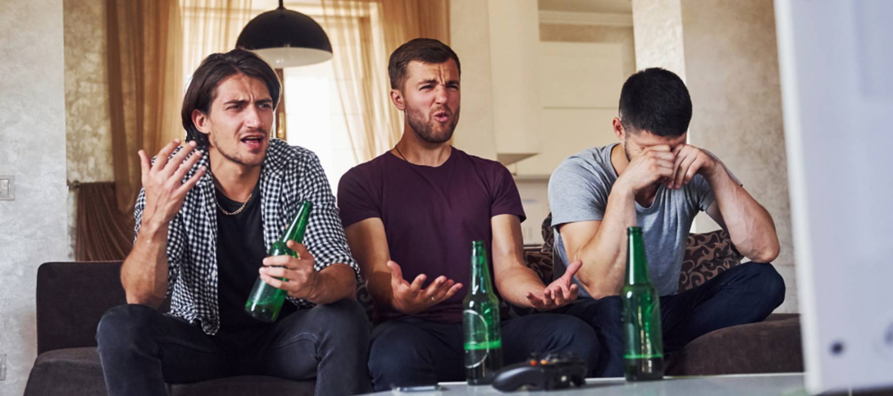 Sad three friends watching soccer on TV at home together on the couch with beers.