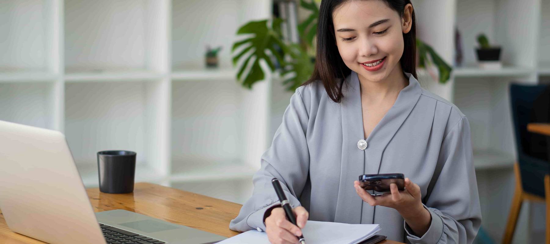 Asian businesswoman holding smartphone with charts or documents at work using business laptop calculator, financial accountant, money calculation, bank, loan, rent, payment.