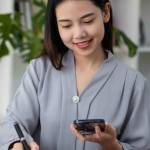 Asian businesswoman holding smartphone with charts or documents at work using business laptop calculator, financial accountant, money calculation, bank, loan, rent, payment.