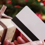 Young woman holding a credit card and a gift box against the background of Christmas decor and gifts, close-up. Christmas and New Year shopping on the Internet, payment by credit card.