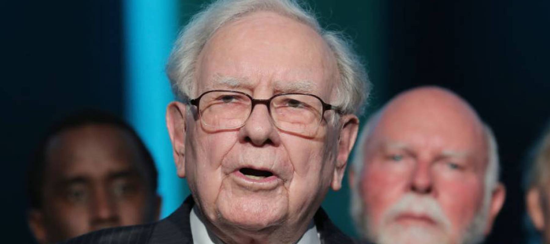 Warren Buffett speaks on stage, making hand gestures.