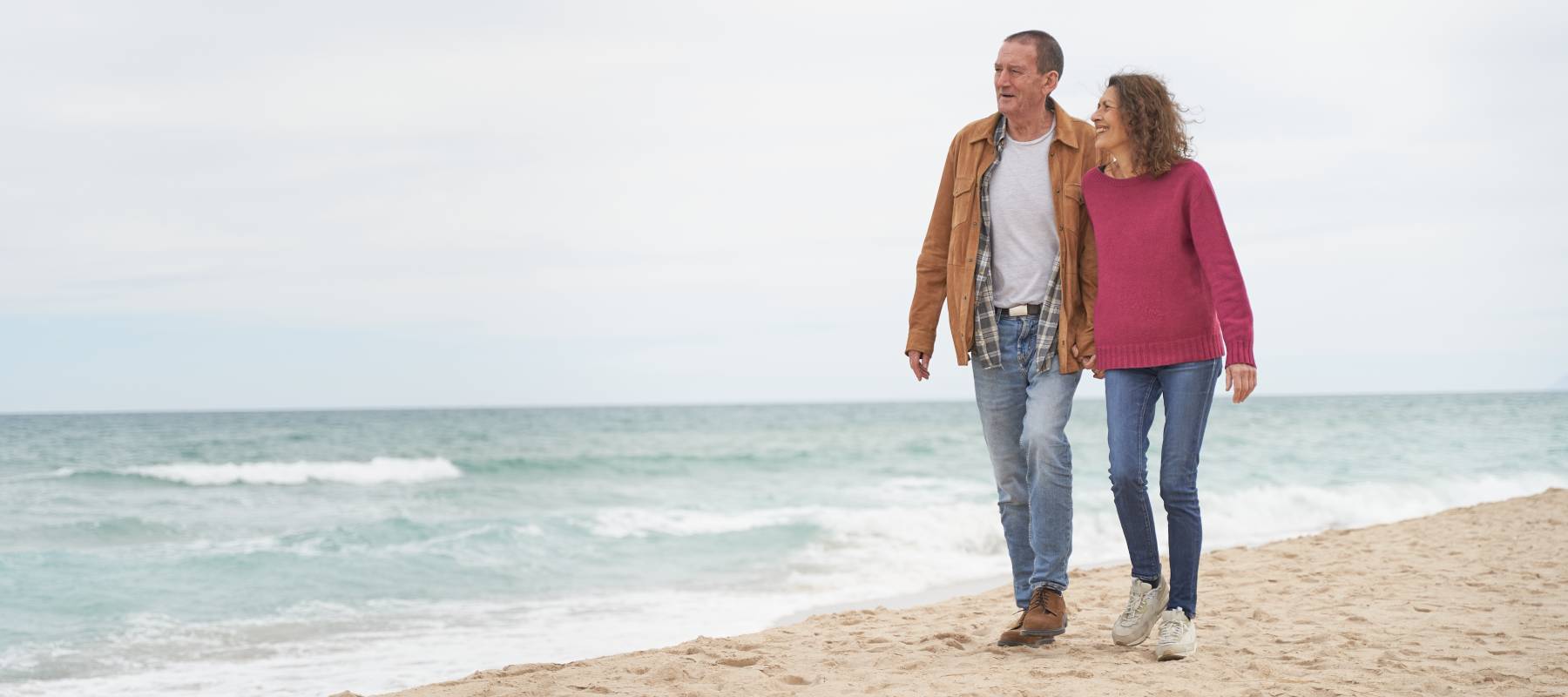 Mature Couple walking in beach sand by the ocean