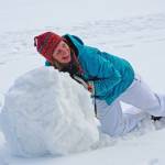 Young college-age woman rolling giant snowball to make snowman.