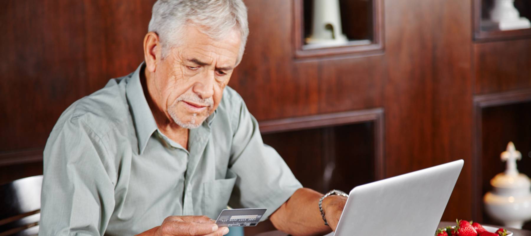 Senior man at laptop paying with credit card for online shopping