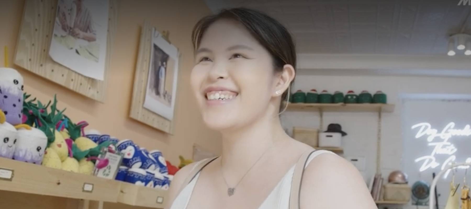 Happy young woman smiles at camera while standing in front of pet toys in a store.
