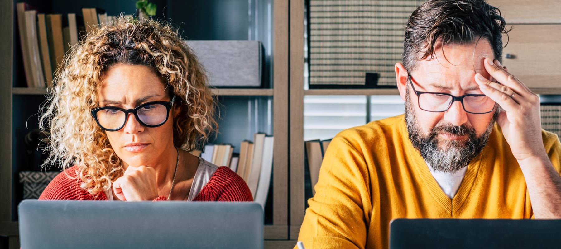 Stressed looking couple look at their computers in the living room.