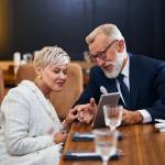 Older Man smiles and shows woman tablet screen during dinner date.