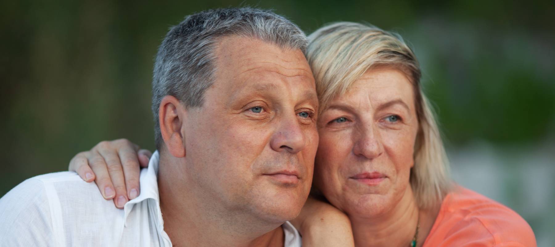 A man in a white shirt and a fair haired woman in an orange one are looking into the distance