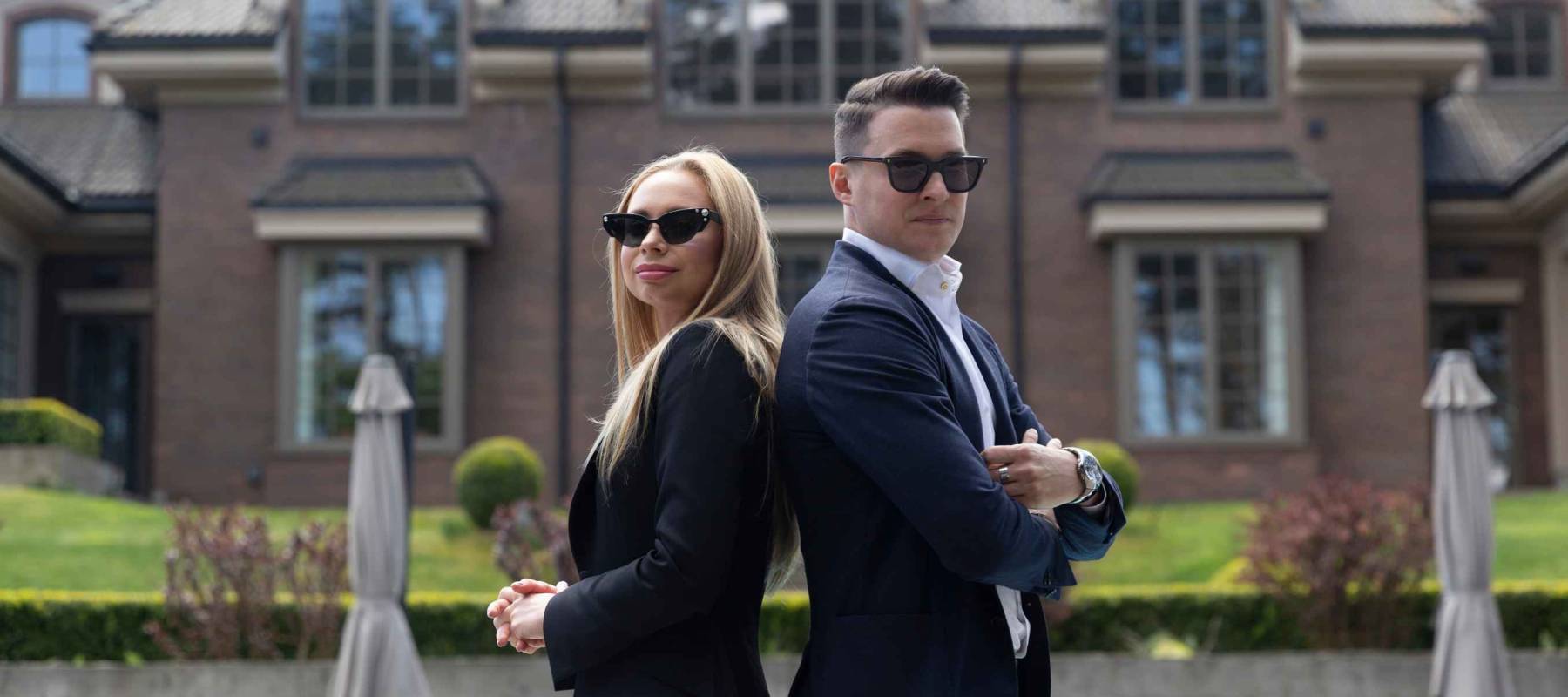 Wealthy couple in front of big house with lit large garden. Man and woman enjoying buying vacation home at estate management company