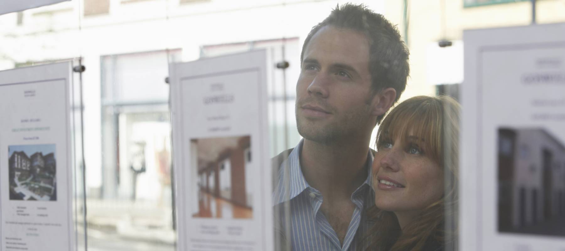 Closeup of a young couple looking through window at estate agents.