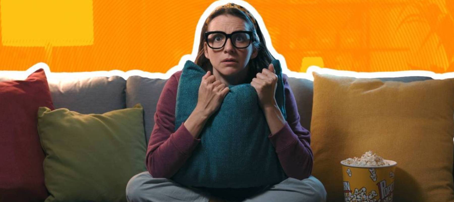 woman in glasses sitting on a couch, holding pillows, looking afraid
