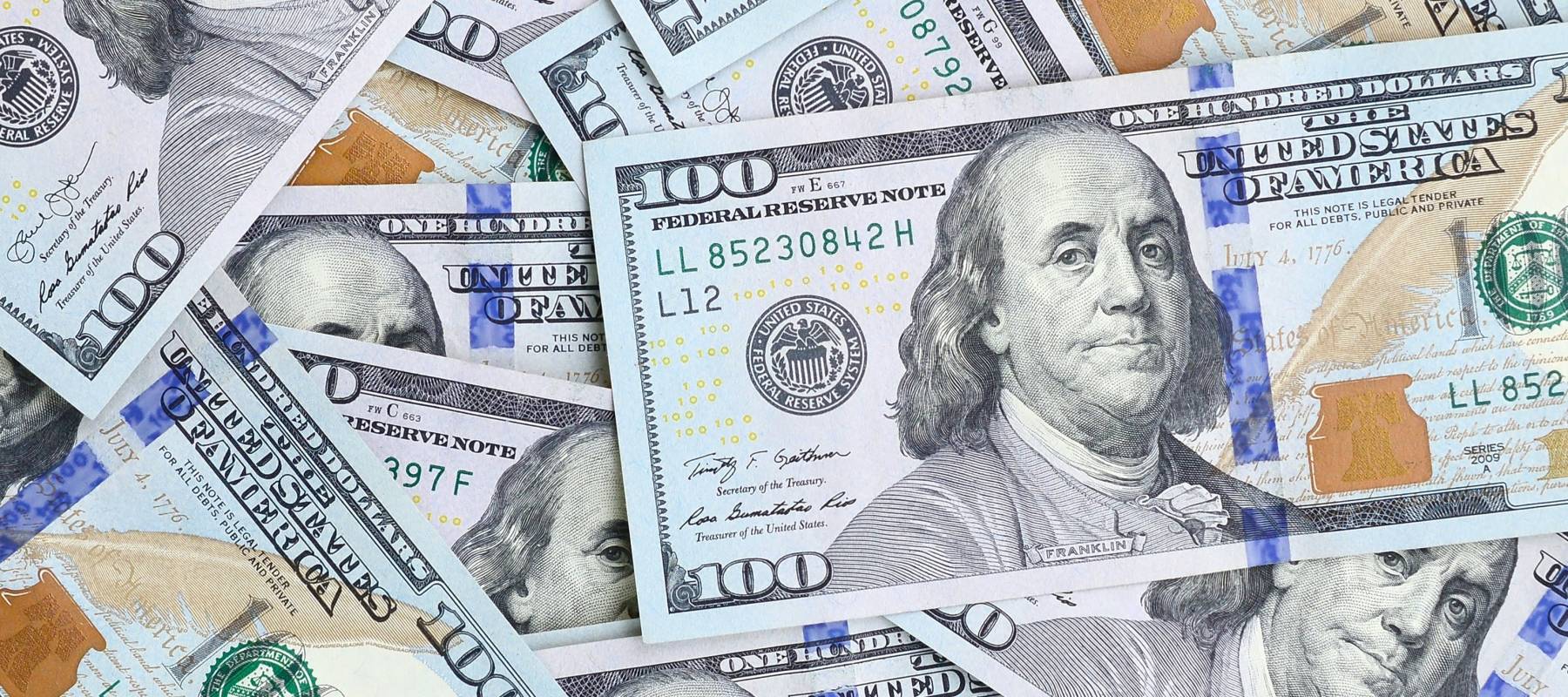 American $100 bills loosely cover a surface