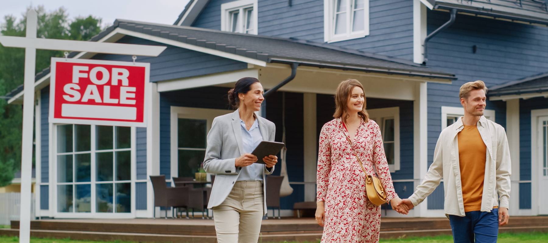Couple and real estate agent talking in front of blue detached home for sale, for sale sign in view.