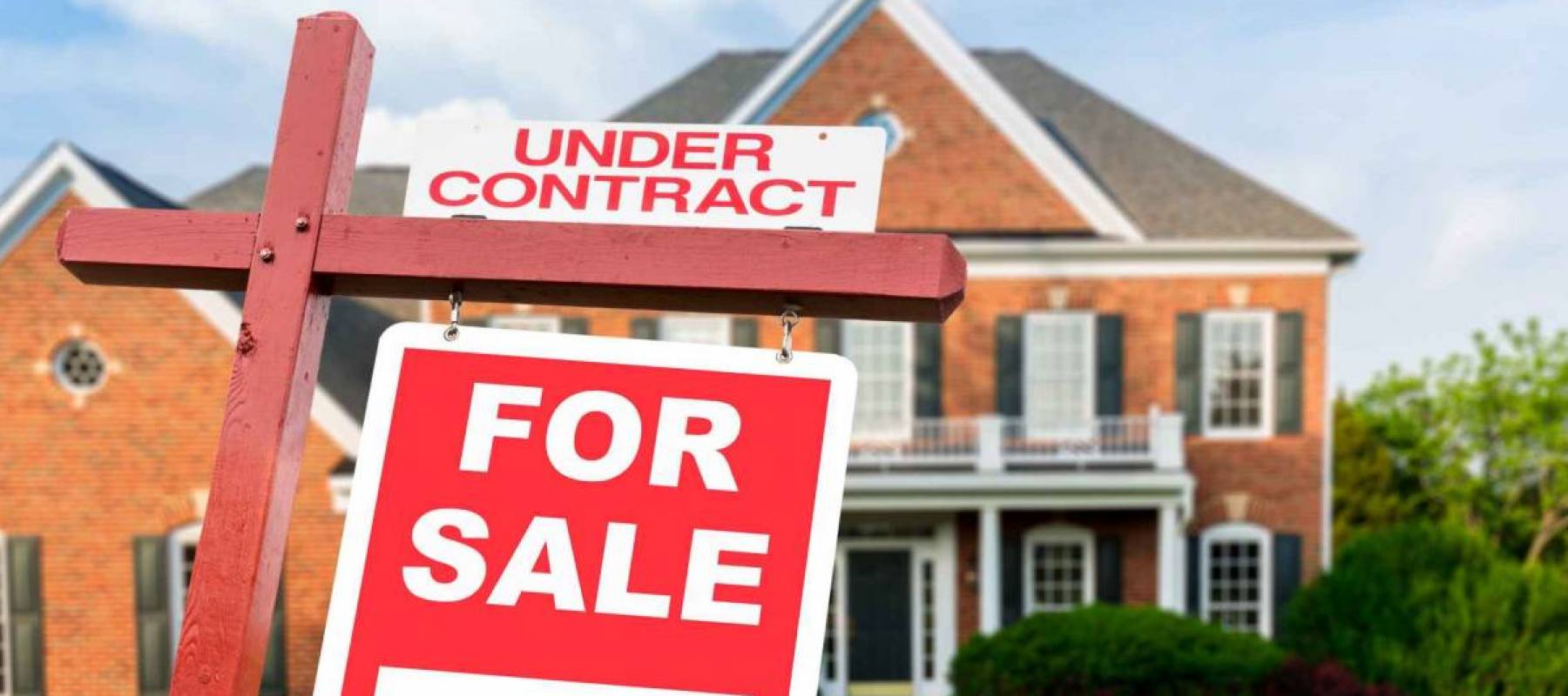 For Sale and Under Contract realtor sign in front of large brick single family house in expansive grass yard for real estate opportunity