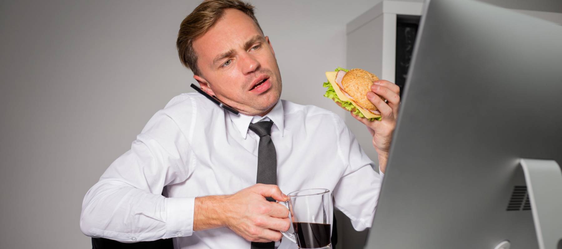 Busy man at the office having coffee and burger.