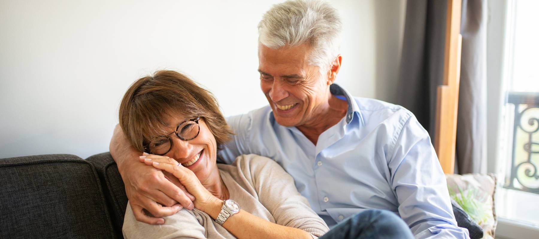 Happy older couple sitting on the couch, smiling and laughing.