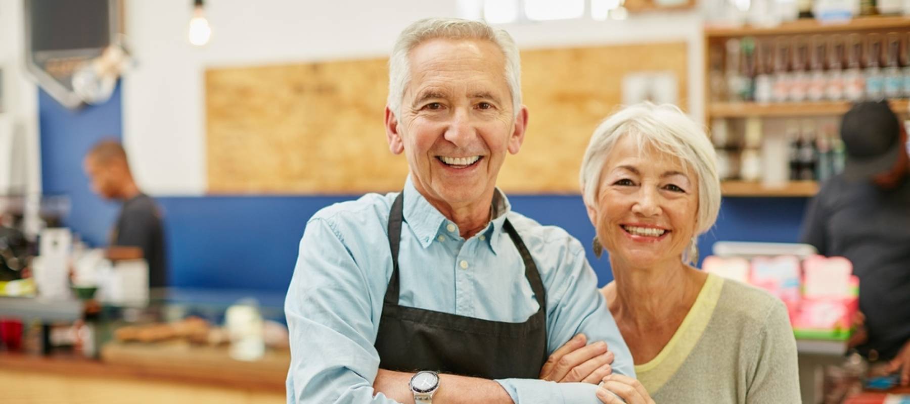 Senior couple running a small business together, standing posed for the camera with smiles and crossed arms.