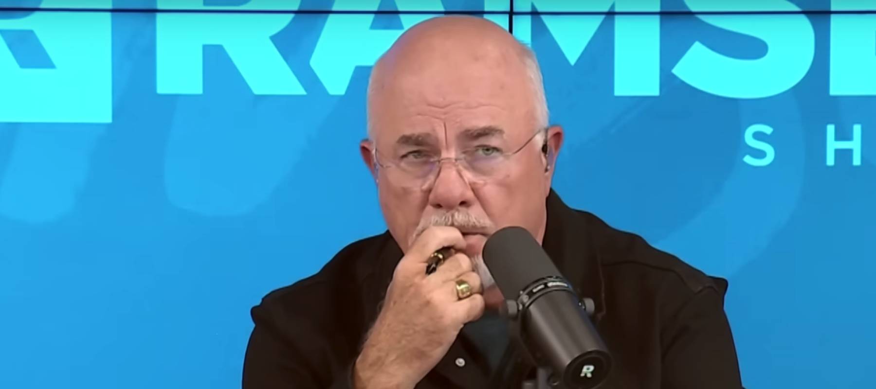 Dave Ramsey on set of his radio show, looking serious and with his hand over his mouth.