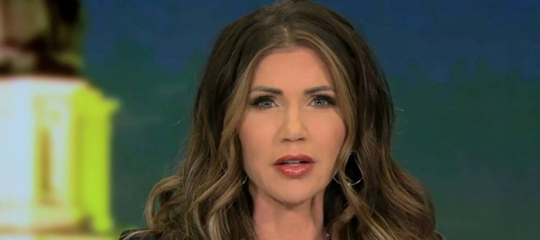 Kristi Noem looks directly at the camera, in the middle of speaking, serious countenance.