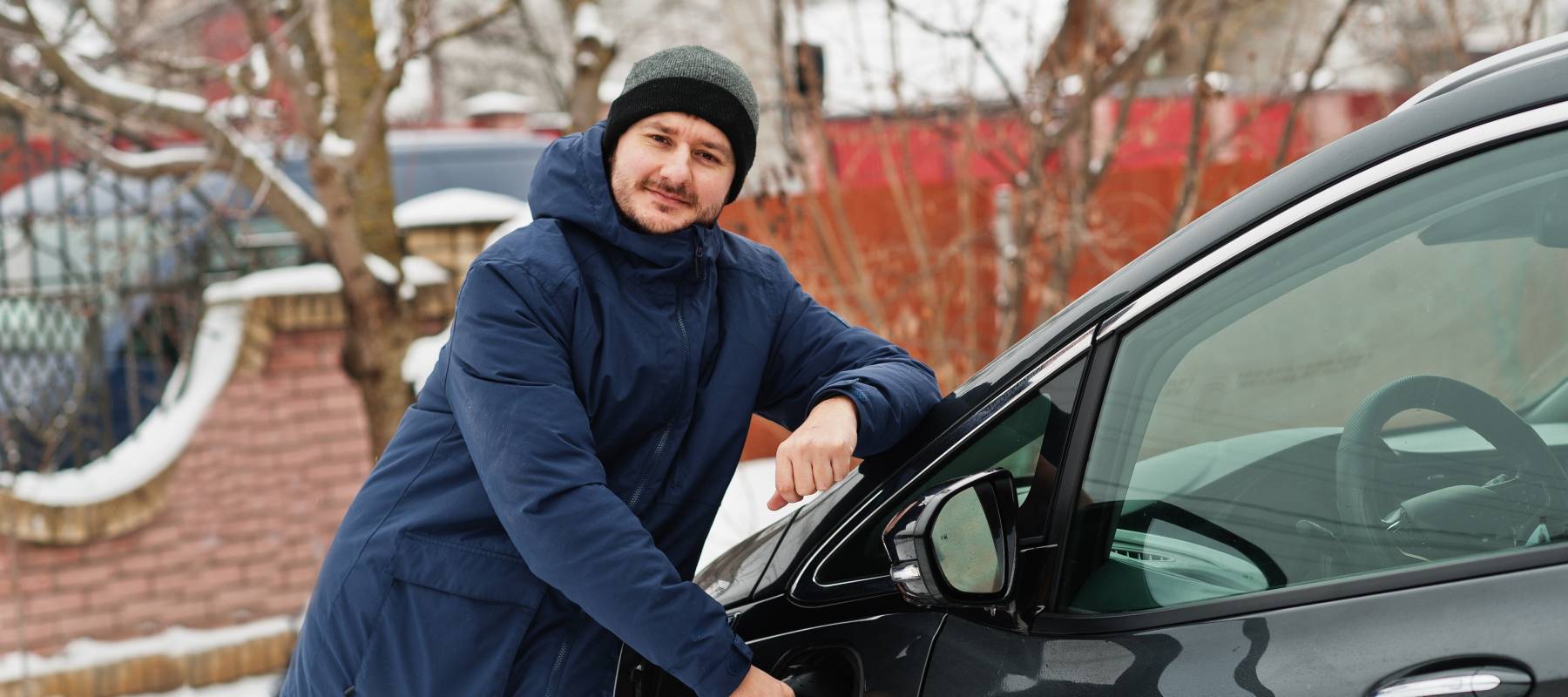 Young man charging his electric car in winter gear.
